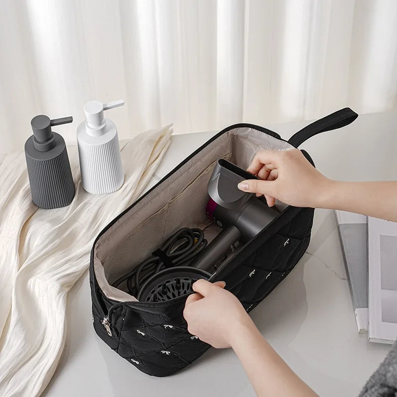 A hand is opening a black storage bag for a portable hair dryer and styling tool.