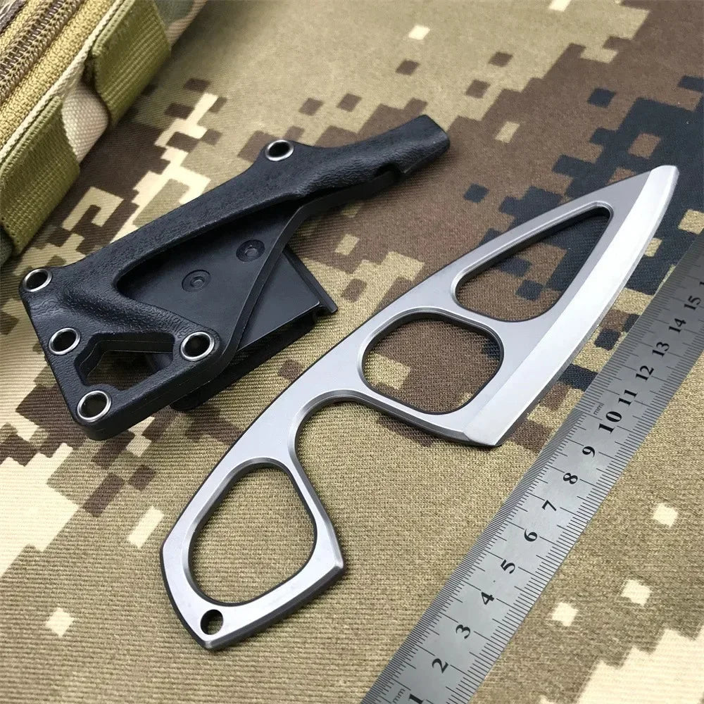 A black fixed-blade neck knife is shown next to a silver measuring ruler on a camouflage background.