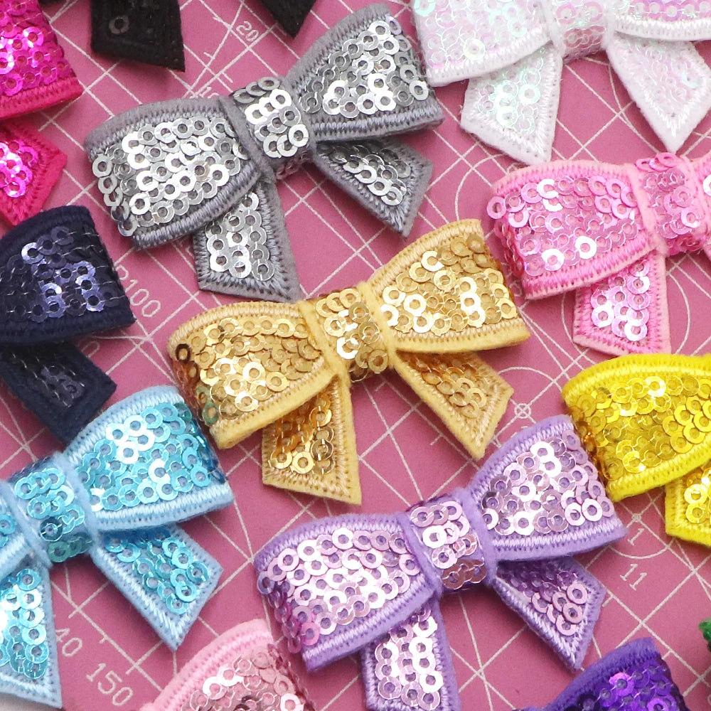 A collection of five sparkly sequin bow patches in various shades including silver, gold, pink, purple, and blue.