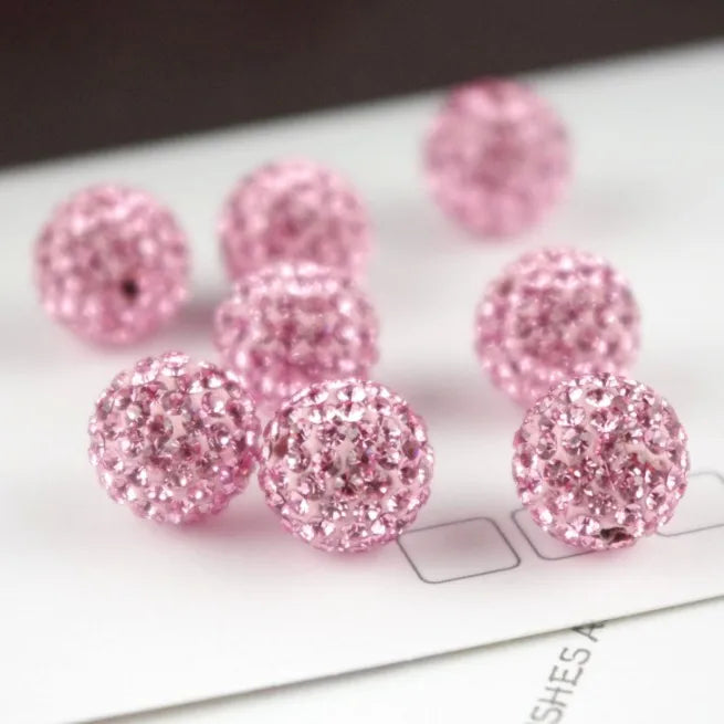 Pink crystal clay round beads scattered on a white surface for DIY jewelry and craft projects