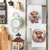 A set of two cute Highland cow kitchen towels featuring floral designs displayed on a wooden rack.
