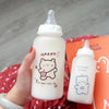 A hand holds a white plastic water bottle with a cute bear design and text on it against an orange background.