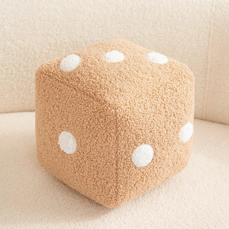 A square beige plush pillow with white polka dots resting on a light surface.