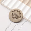 A round, tan label with an embossed heart design is placed on a piece of white paper.