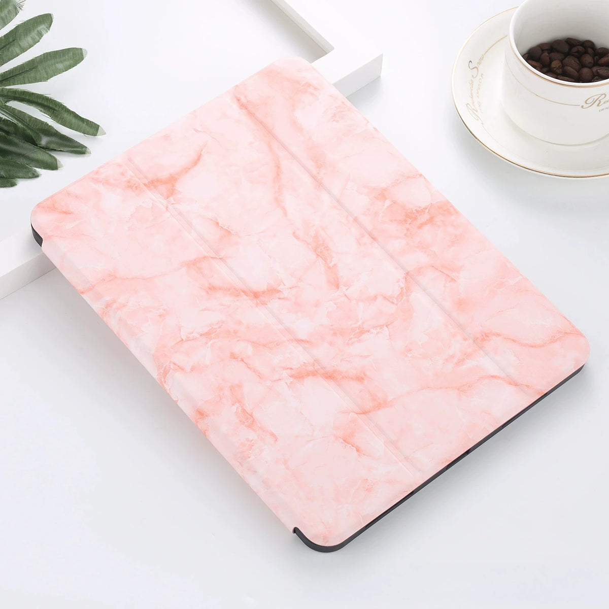 A pink marble patterned case for an iPad Pro with a built-in pencil holder resting on a white surface.