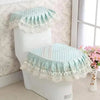 A white toilet seat is covered with a light mint green lace and sheer fabric cushion set.