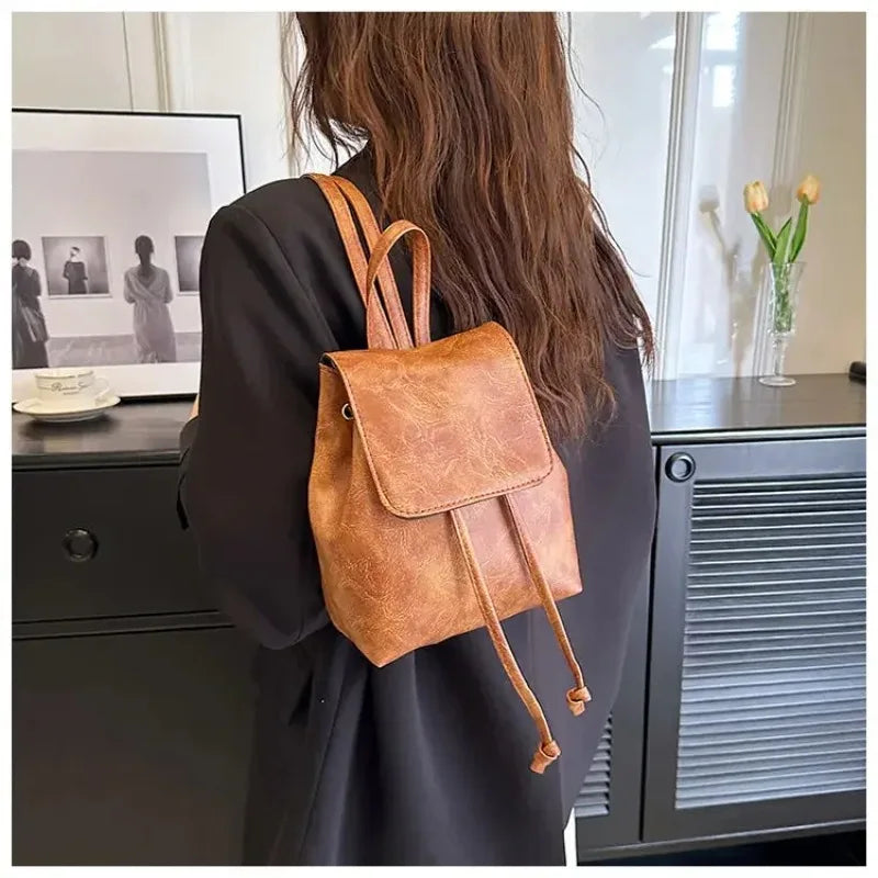 Une personne tient un mini sac à fermeture à cordon marron artistique dans un blazer sombre, à côté d'un verre et d'une armoi