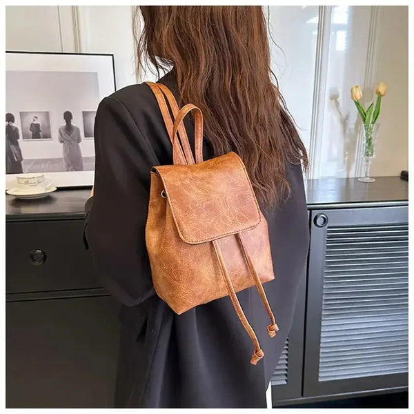 Une personne tient un mini sac à fermeture à cordon marron artistique dans un blazer sombre, à côté d'un verre et d'une armoi