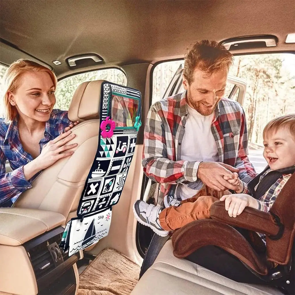 A father and daughter look at a high-contrast crinkle cloth book with a tummy time mirror in a car seat.