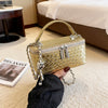 A hand holds a gold woven PU leather crossbody bag with a chain strap on a light carpet.