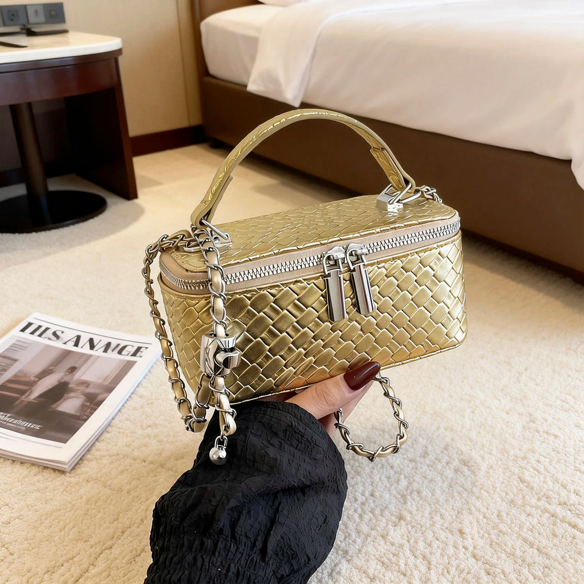 A hand holds a gold woven PU leather crossbody bag with a chain strap on a light carpet.