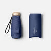 A dark blue pocket-size folding umbrella with a light-colored handle and UV protection text on the sleeve.