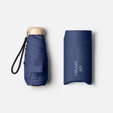 A dark blue pocket-size folding umbrella with a light-colored handle and UV protection text on the sleeve.