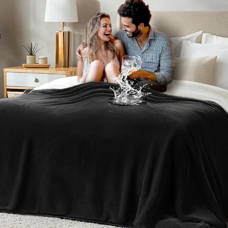 A smiling couple laughing while playfully splashing water on a black flannel blanket in a bedroom setting.