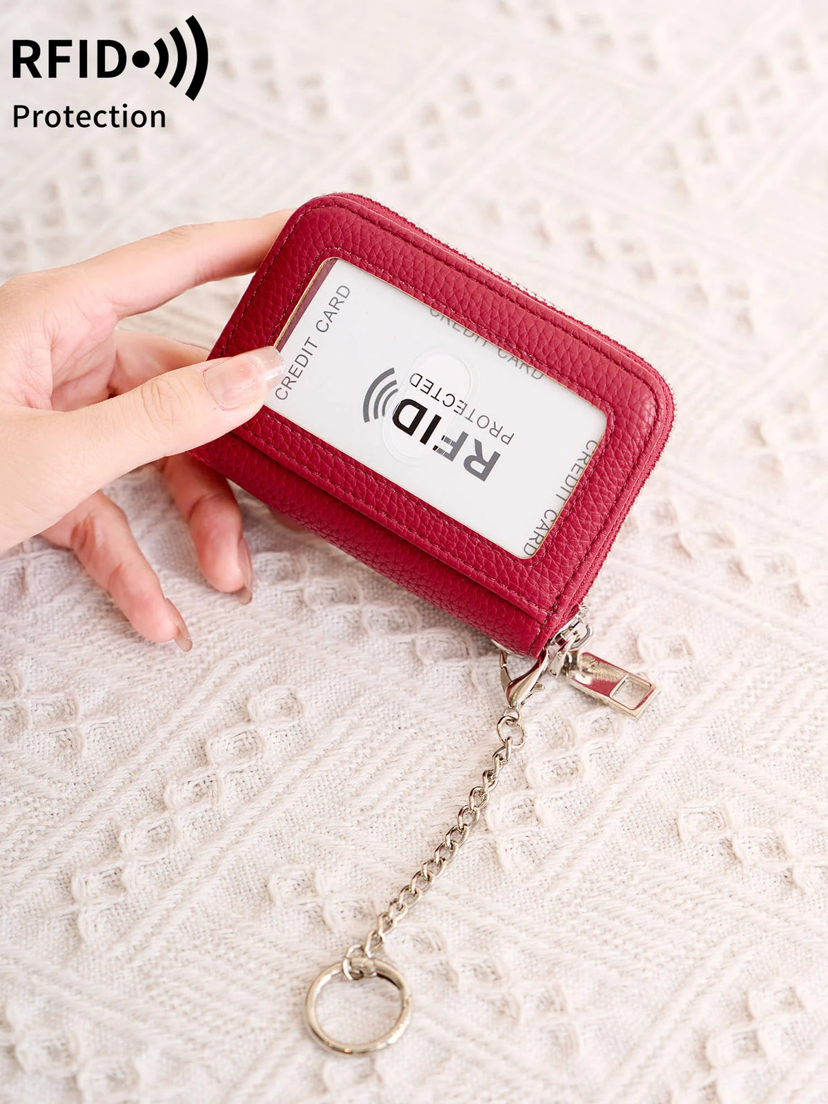 A hand holds a red accordion wallet with an RFID protected credit card inside, attached to a silver chain.