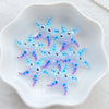 A collection of small, iridescent blue and purple starfish resin charms on a white dish.