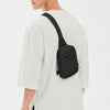 A man wearing a white t-shirt and olive pants holds a black 2-in-1 convertible waist and crossbody sling bag.