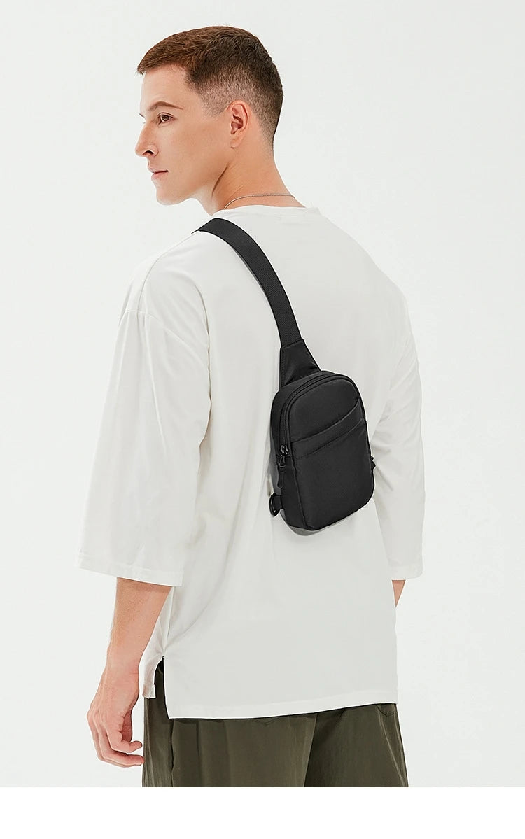 A man wearing a white t-shirt and olive pants holds a black 2-in-1 convertible waist and crossbody sling bag.
