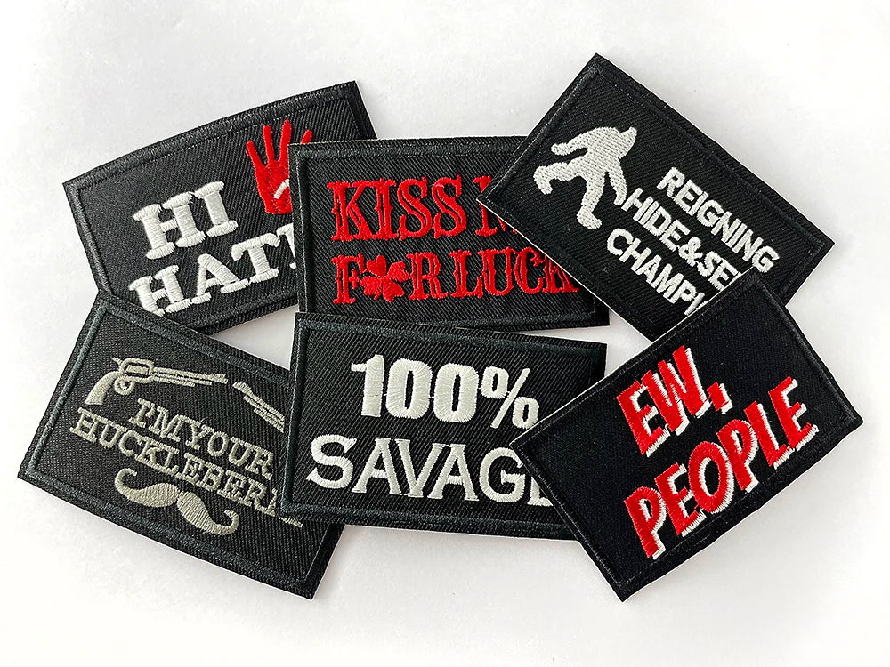 A collection of black embroidered iron-on patches featuring humorous text like HI HAT and Savage