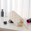 A beige quilted storage bag for a portable hair dryer or styling tool, resting on a white surface next to soap dispensers.
