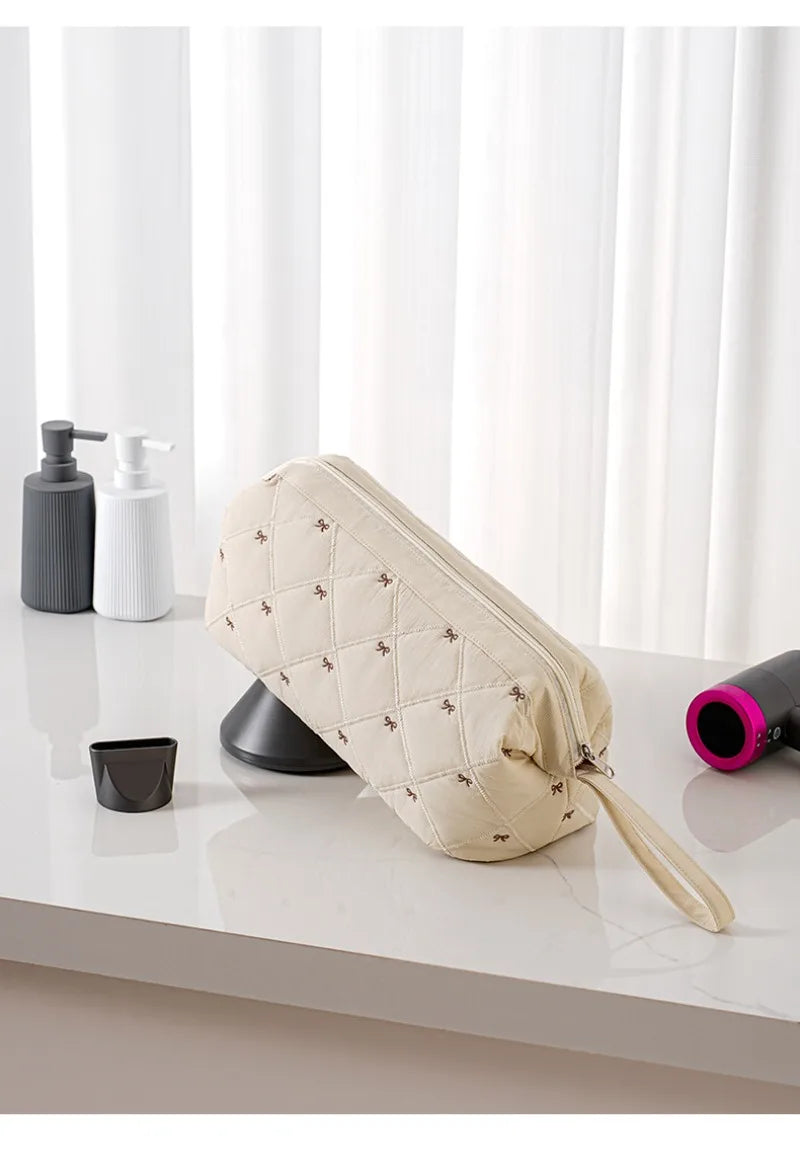 A beige quilted storage bag for a portable hair dryer or styling tool, resting on a white surface next to soap dispensers.