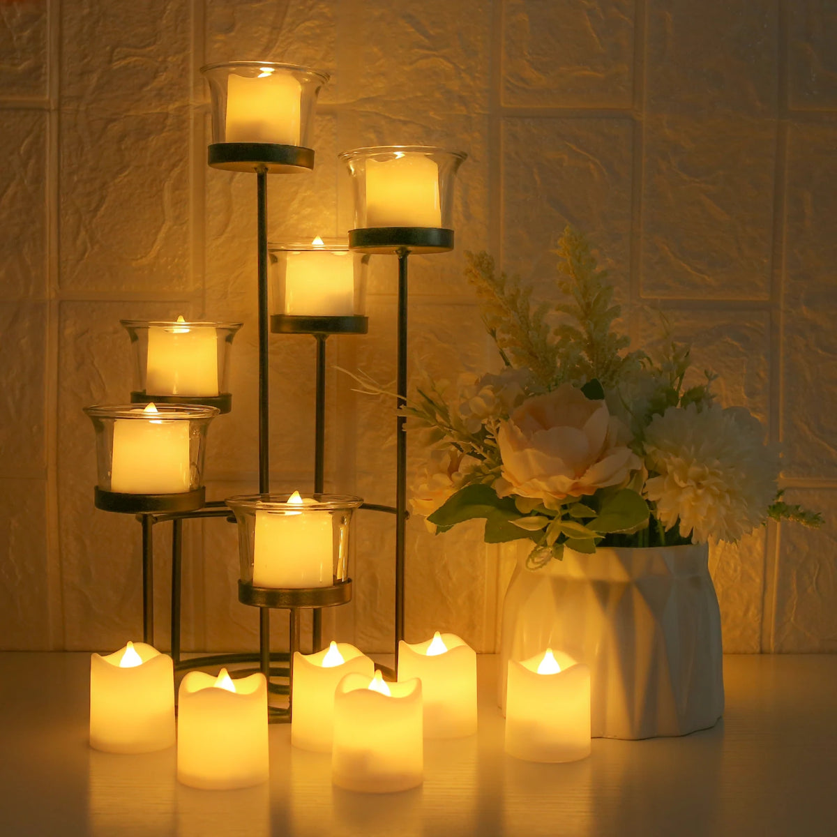 A collection of glowing LED tea lights in glass holders are displayed on a wooden surface against a textured wall.
