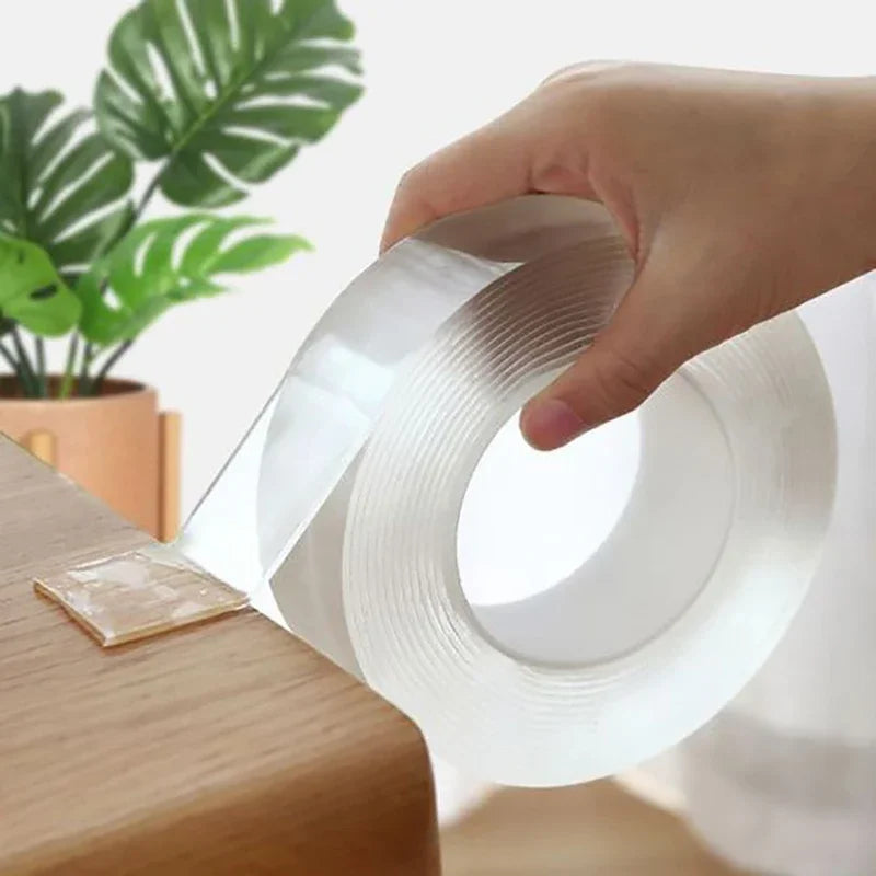 Une main tient un rouleau de ruban adhésif nano transparent à double face devant un fond de plante verte flou.
