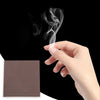 A hand is blowing smoke from a piece of brown chemical smoke magic paper against a black background.