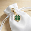 Gold-toned four-leaf clover charm attached to a white fabric drawstring bag