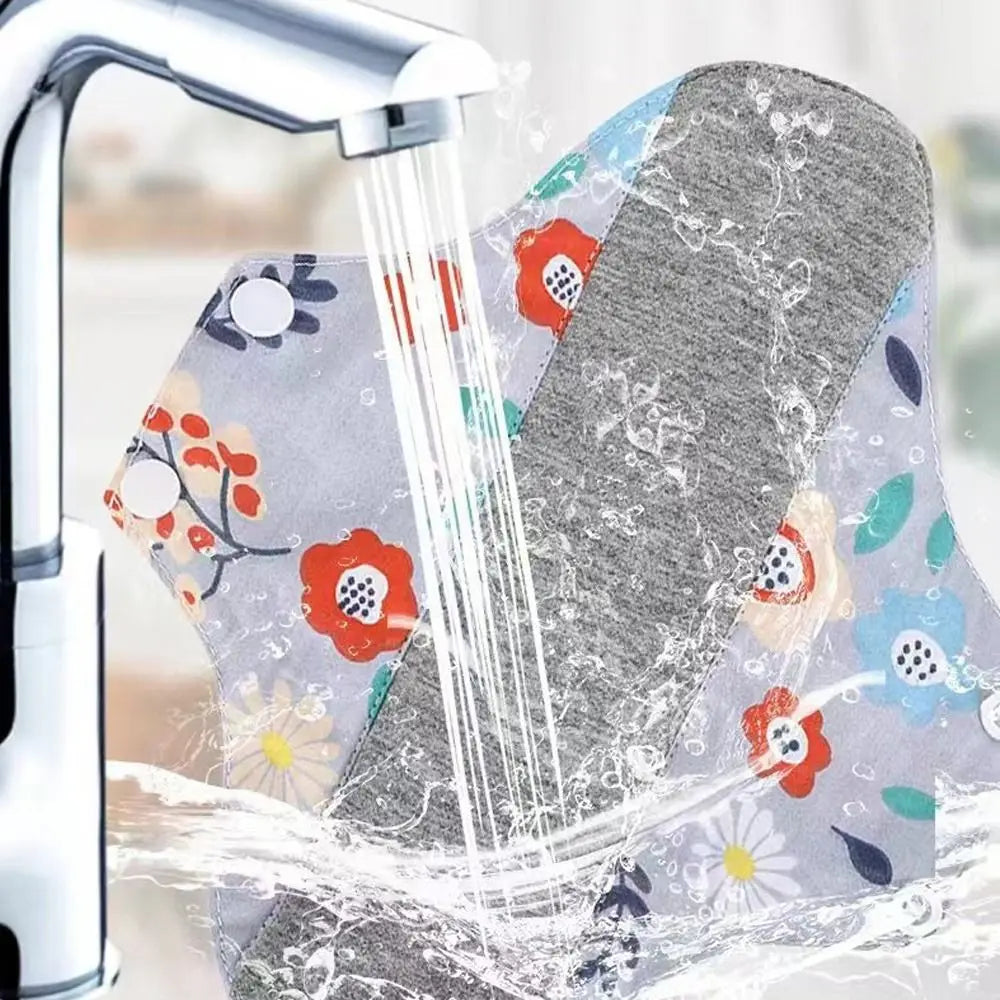 Reusable cotton menstrual pads being rinsed under a faucet with water flowing over them.