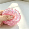 Eine Hand hält ein rosa glitzerndes Dumpling-Squishy Fidget-Spielzeug vor einem weißen Hintergrund.