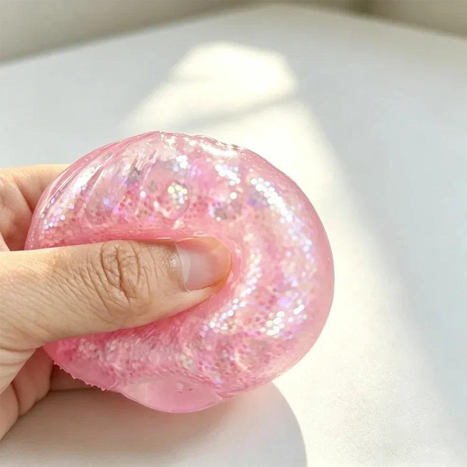 Eine Hand hält ein rosa glitzerndes Dumpling-Squishy Fidget-Spielzeug vor einem weißen Hintergrund.