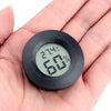 A hand holds a black mini digital hygrometer thermometer displaying 27.4°C and 60% humidity.