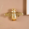 Golden bee-shaped resin wall decor mounted on a beige wall.