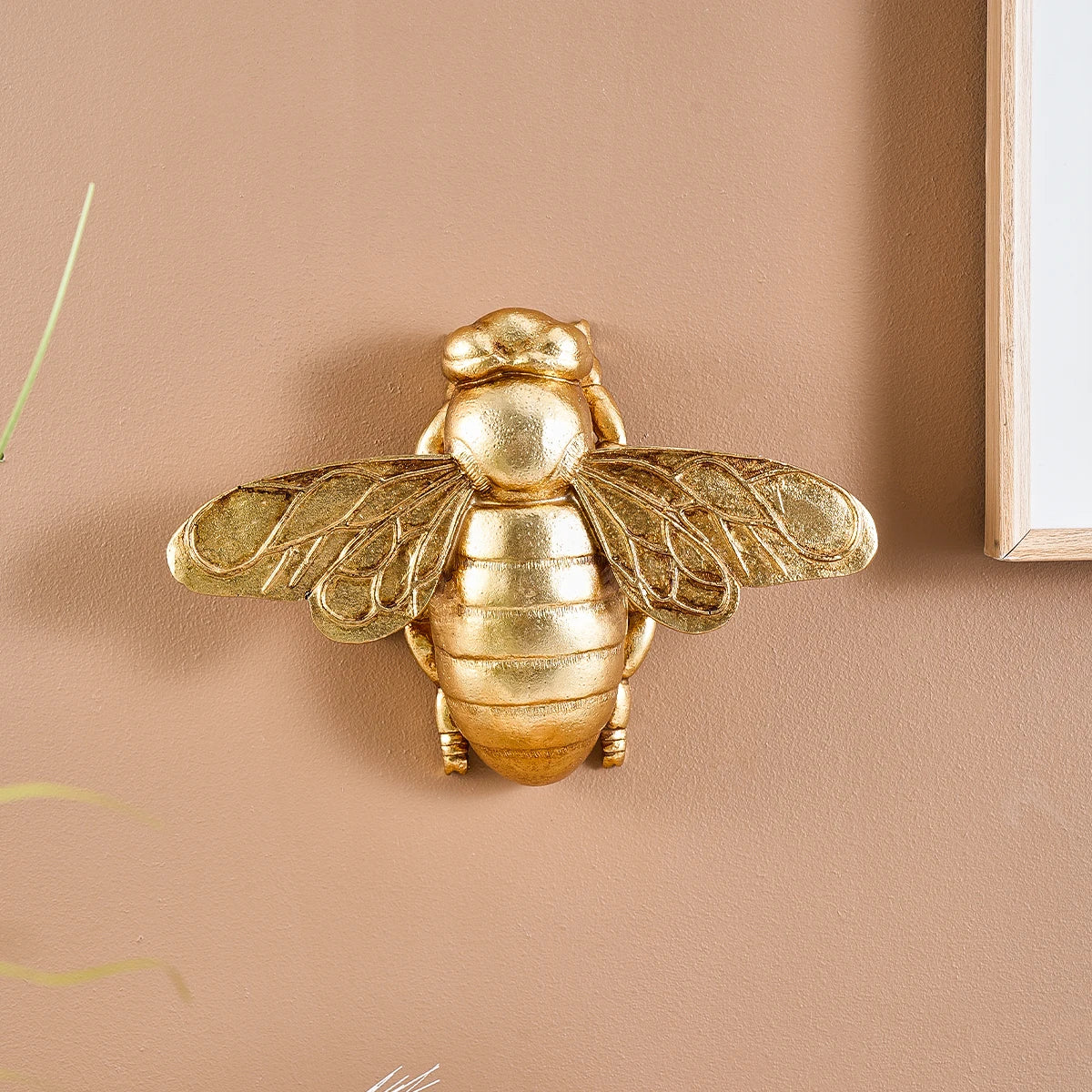 Golden bee-shaped resin wall decor mounted on a beige wall.