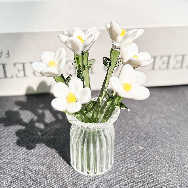 A small glass vase holds a bouquet of white eternal flowers against a light background.