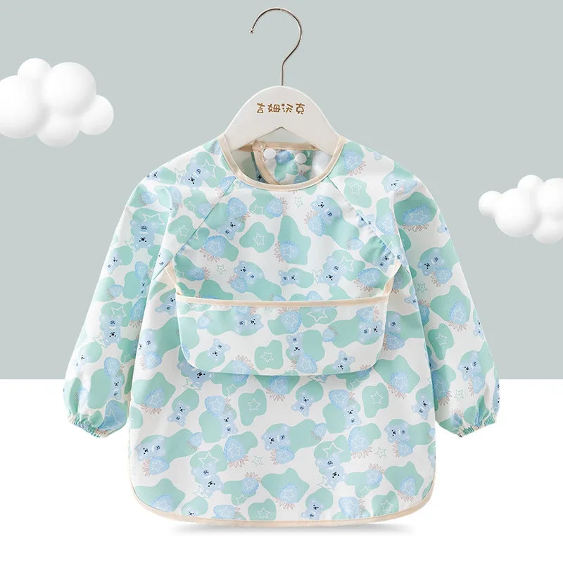 A light blue and green floral patterned children's waterproof long sleeve feeding bib with a catch pocket hanging on a hanger