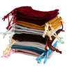 A stack of velvet drawstring jewelry pouches in various shades including maroon, gold, gray, brown, and blue.