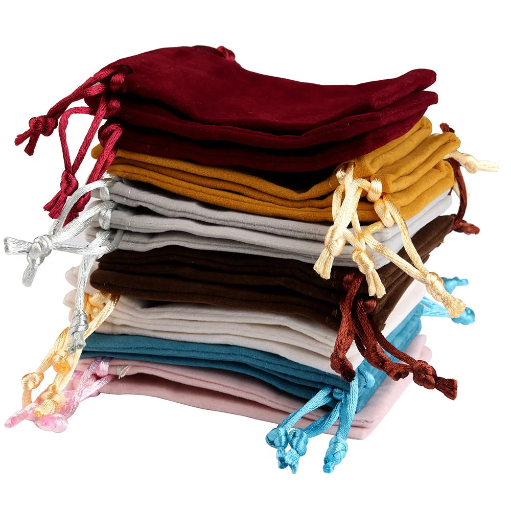 A stack of velvet drawstring jewelry pouches in various shades including maroon, gold, gray, brown, and blue.