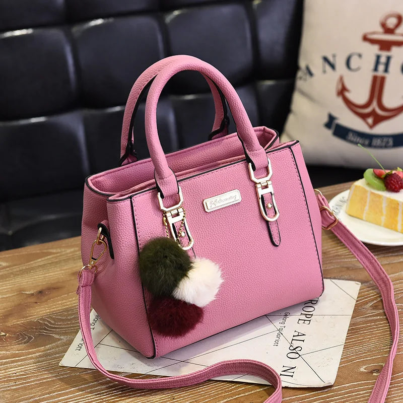 A pink vintage PU leather tassel shoulder bag with a gold-toned strap resting on a wooden surface.