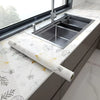 A stainless steel kitchen sink installed in a modern cabinet with white marble peel-and-stick wallpaper.
