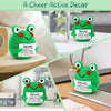Handmade crochet frog doll in green with a positive message card on a wooden surface.