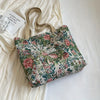 A floral patterned corduroy tote bag resting on a white surface next to a piece of light-colored fabric.