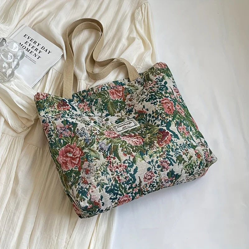 A floral patterned corduroy tote bag resting on a white surface next to a piece of light-colored fabric.