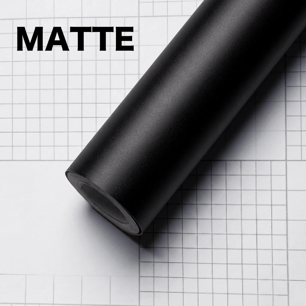 A roll of matte black carbon fiber vinyl wrap film lying on a white grid surface.