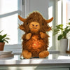 A fluffy brown Highland cow plush toy with breathing motion and light sitting on a white surface.