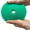 A hand holds a bright green car polishing sponge pad with a circular hole.