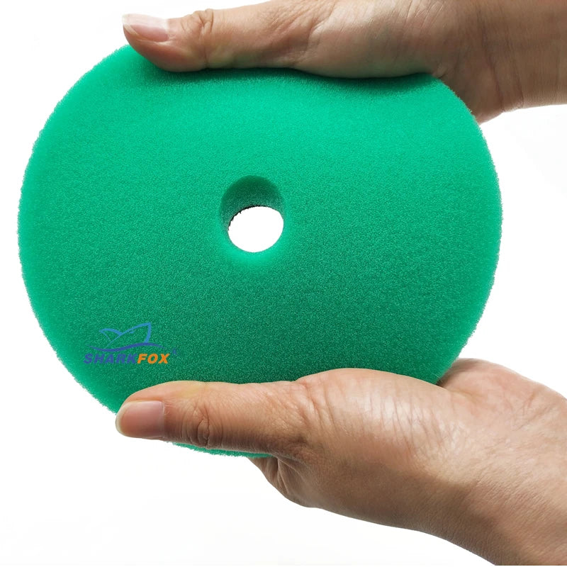 A hand holds a bright green car polishing sponge pad with a circular hole.