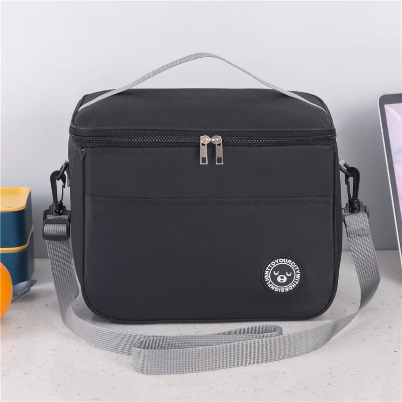 Black thermal insulated lunch bag with an adjustable shoulder strap resting on a white surface.