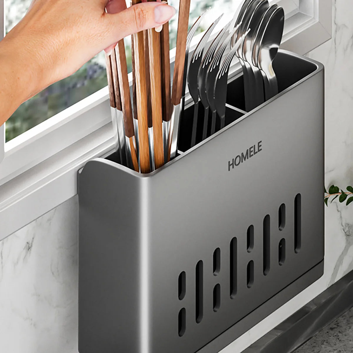 A hand is placing wooden and metal cutlery into a sleek, gray plastic organizer with a drain tray.